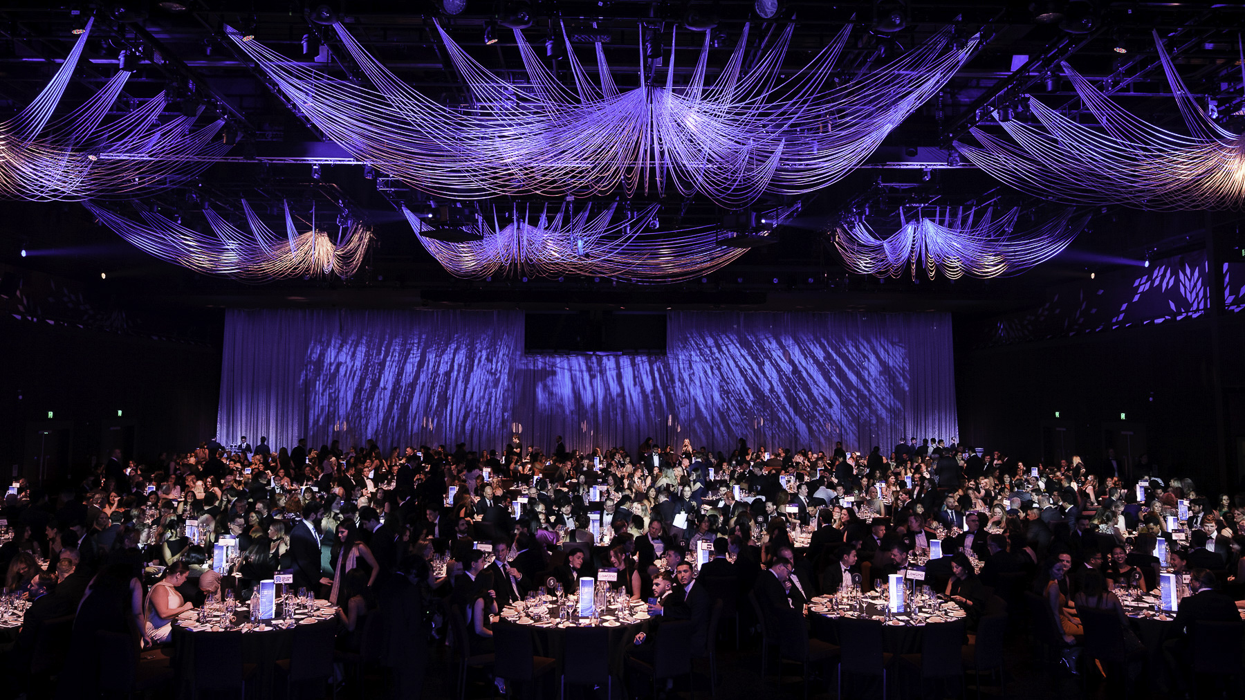 A packed formal awards gala beneath sweeping blue, violet and magenta light installations
